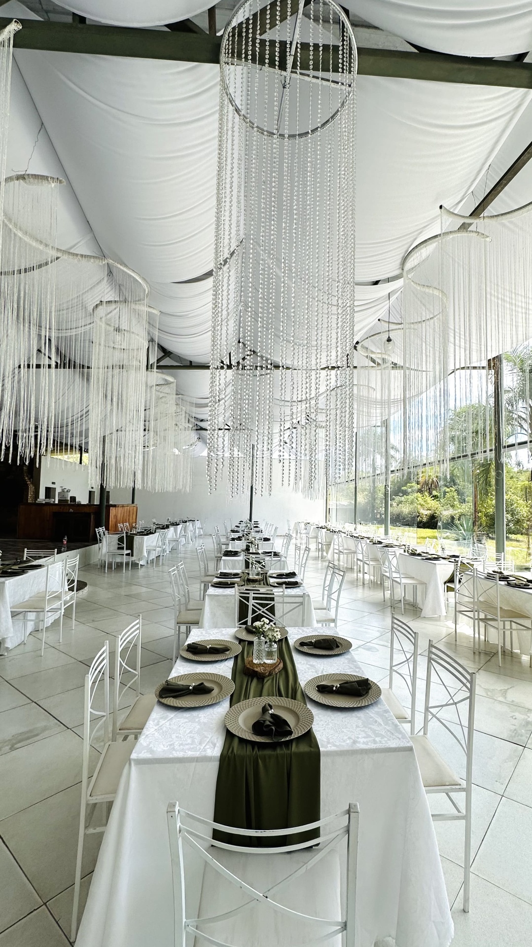 Salão com lustres de cristal e mesas longas decoradas em verde-oliva