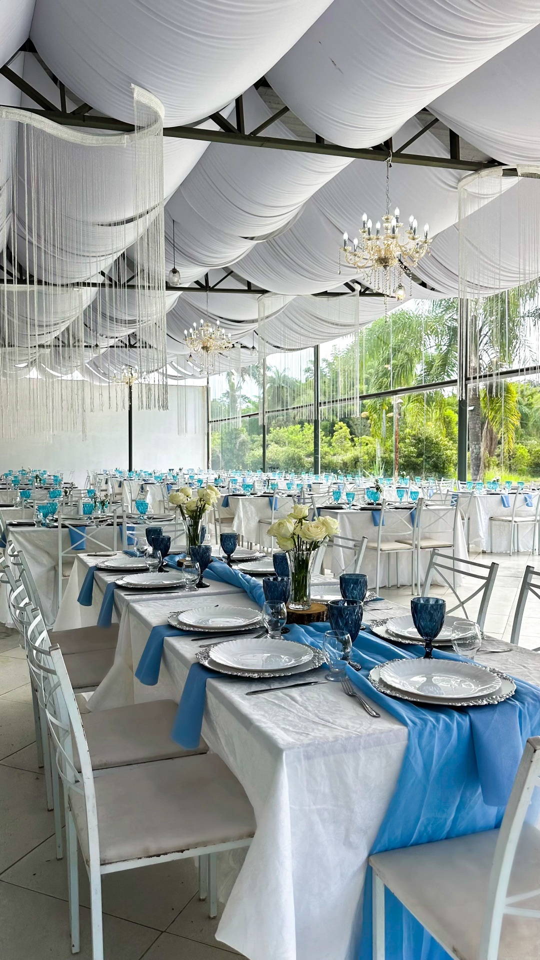 Salão decorado em azul serenity com taças turquesa e vista para as palmeiras