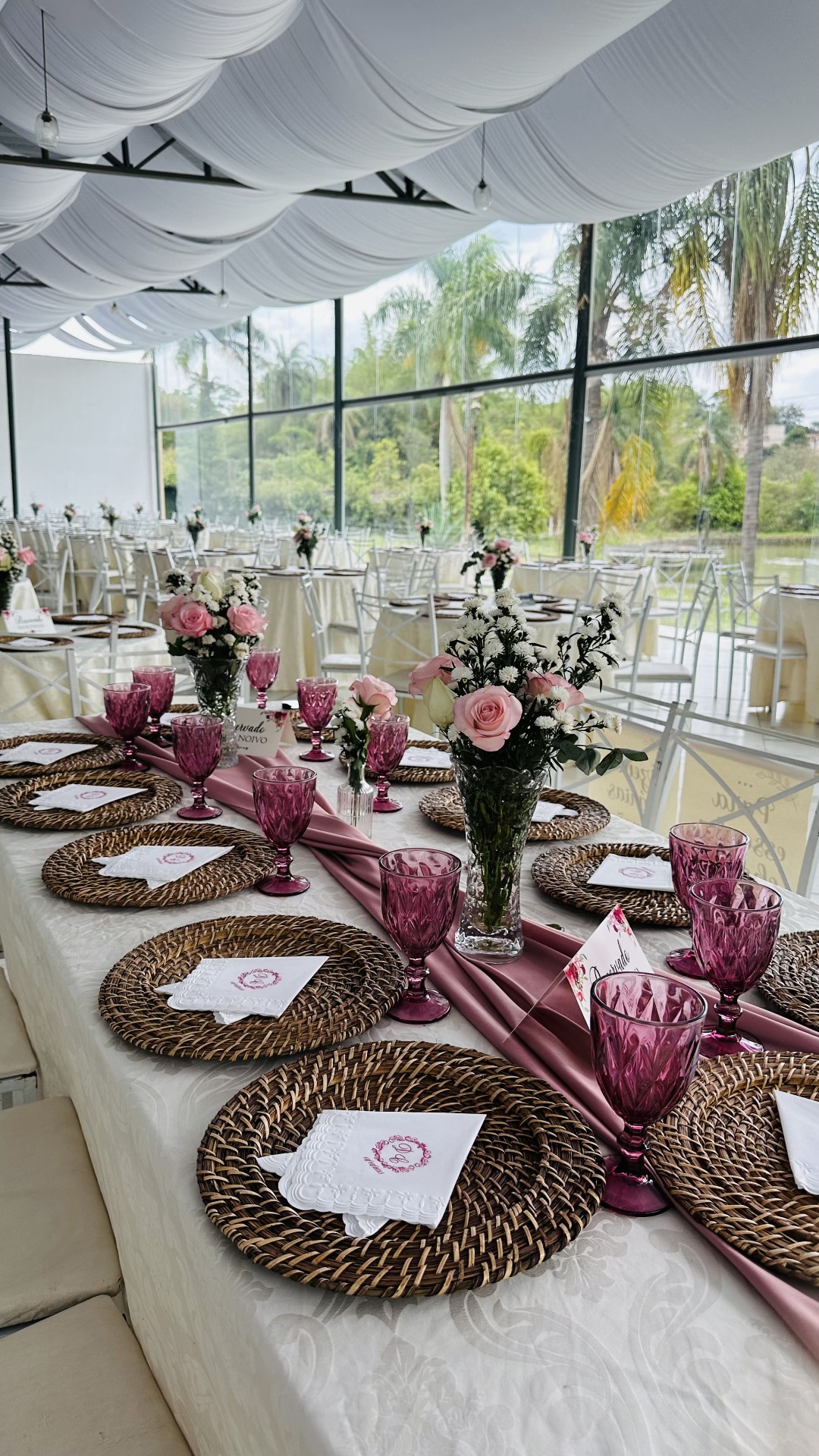 Mesa imperial com runner rosé, taças cor de vinho e arranjos de rosas cor-de-rosa